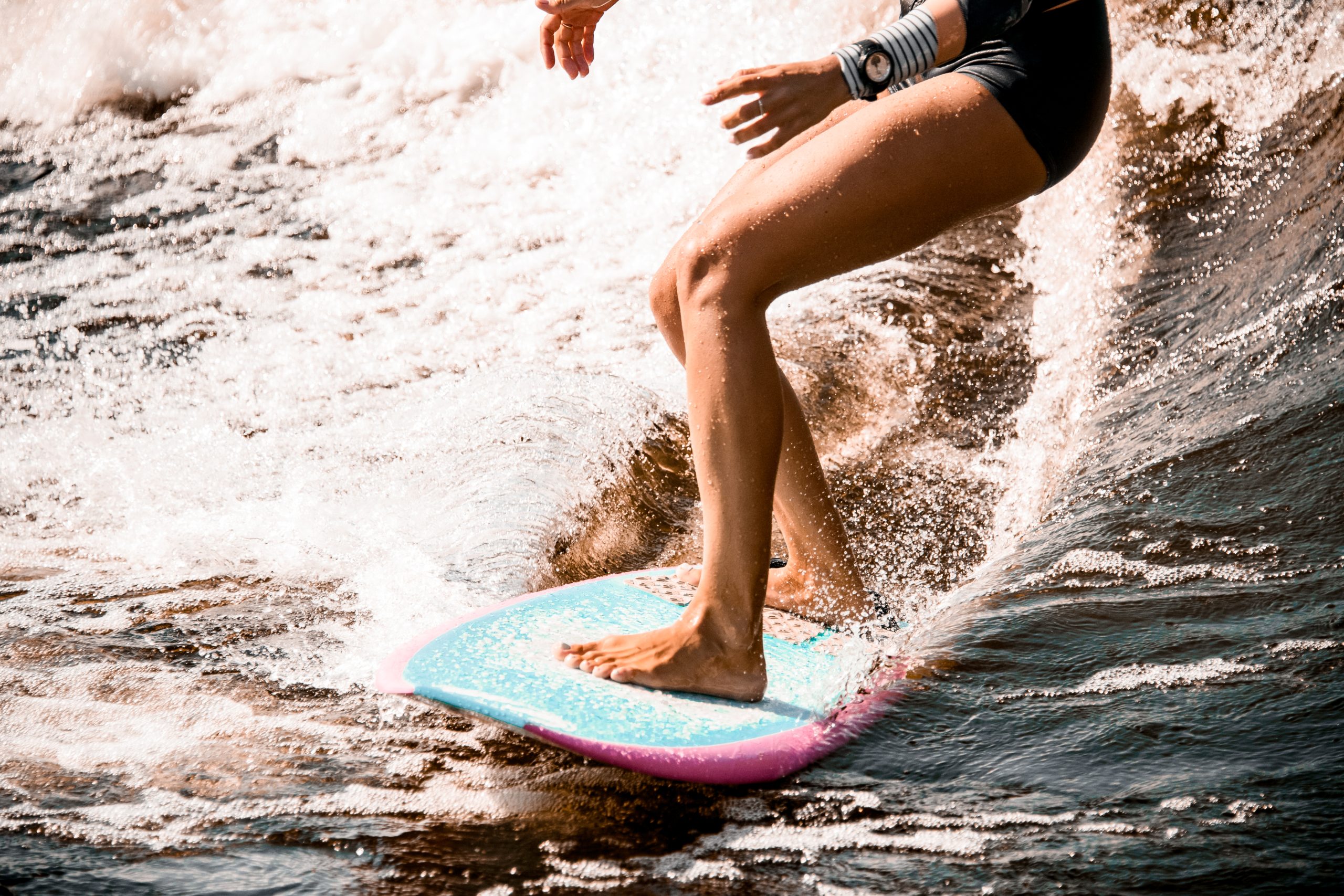 Un primer plano de las piernas de una persona que está haciendo surf con agua que salpica detrás de la tabla de surf.