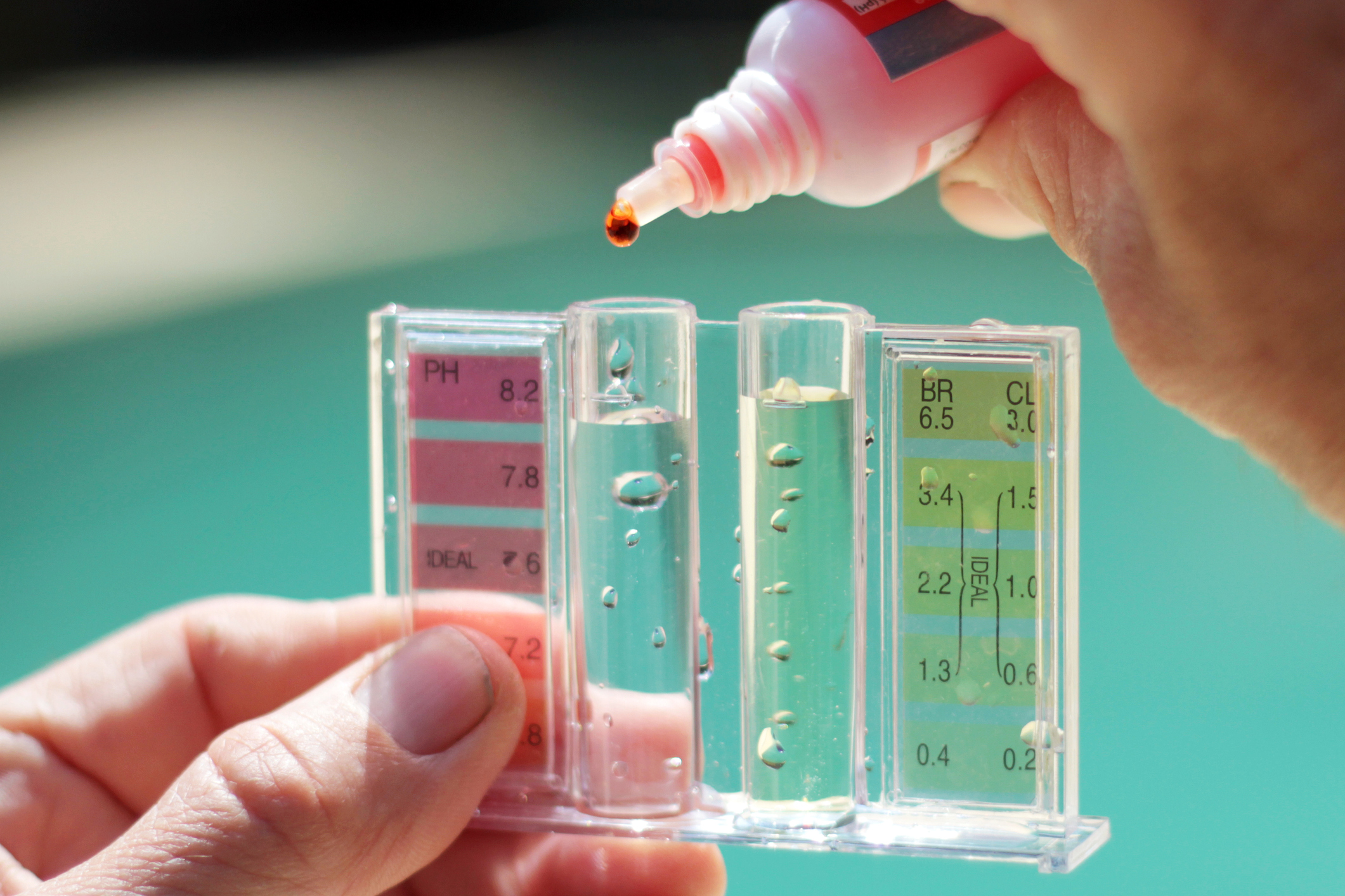 Primer plano de las manos de una persona sosteniendo un dispositivo para analizar cloro frente a un cuerpo de agua.