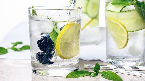 Vasos de agua con limón, pepino, albahaca y moras negras.