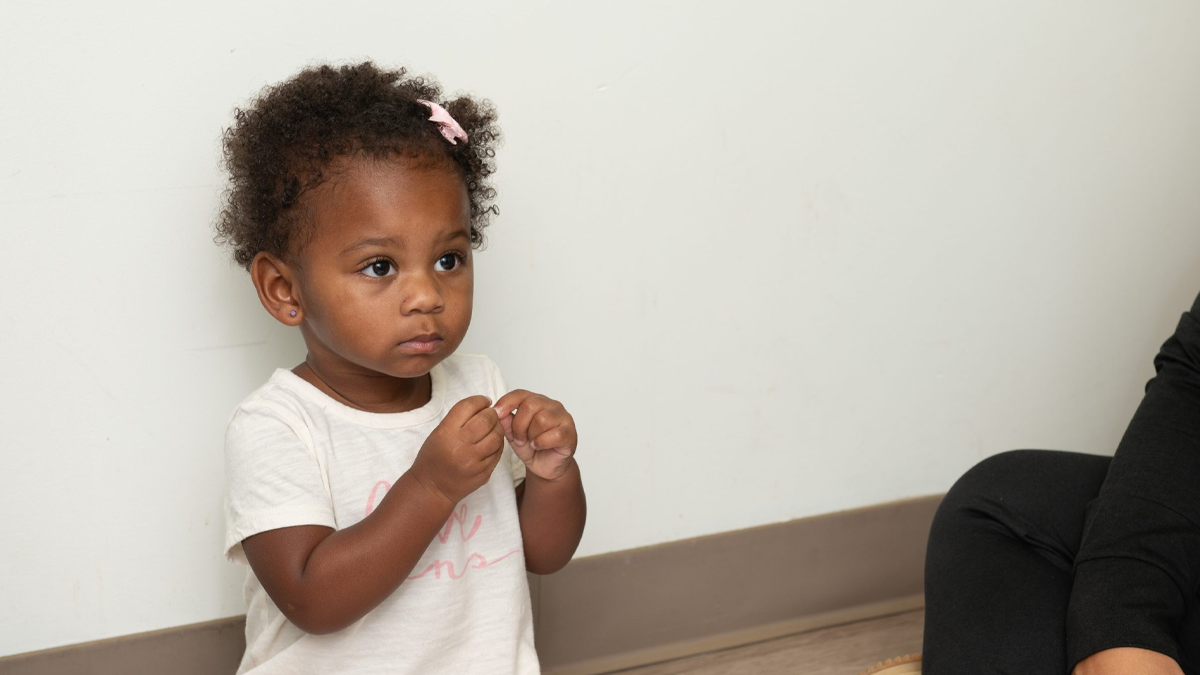 baby sitting on the bed with their mother Toddler using American Sign Language