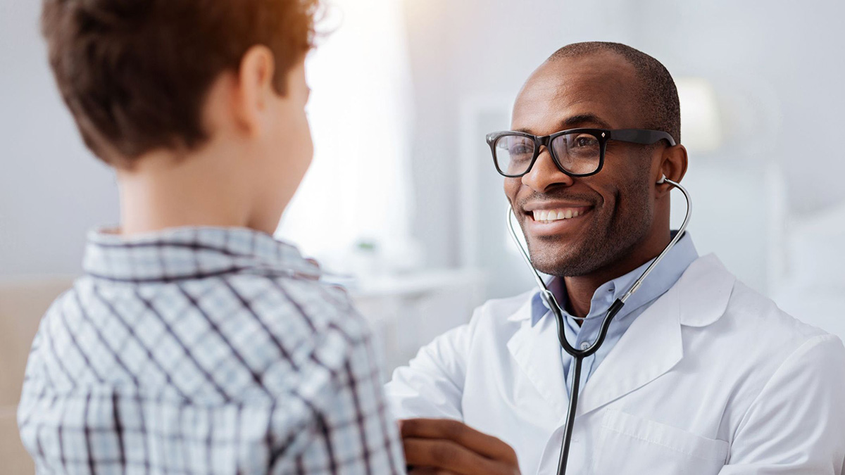 A pediatrician in a lab coat using a stethoscope to listen to a child’s heart.