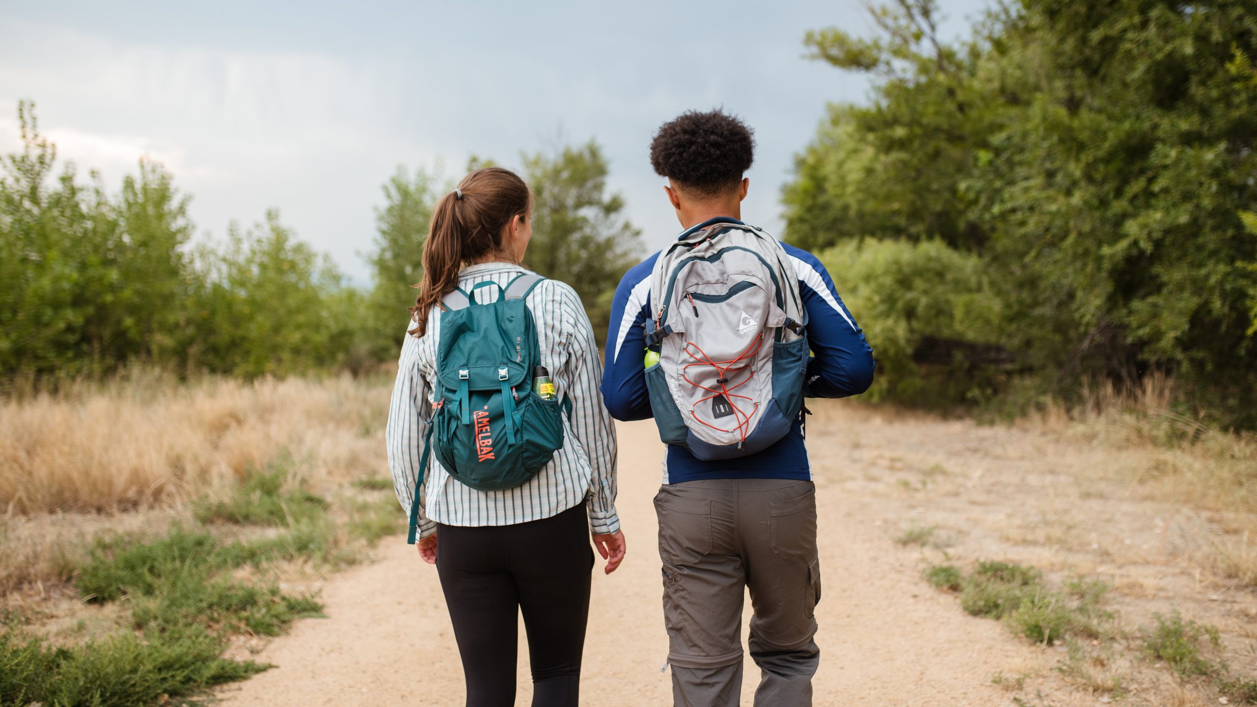 A woman and a man walking on a trail wearing day packs on a hike.