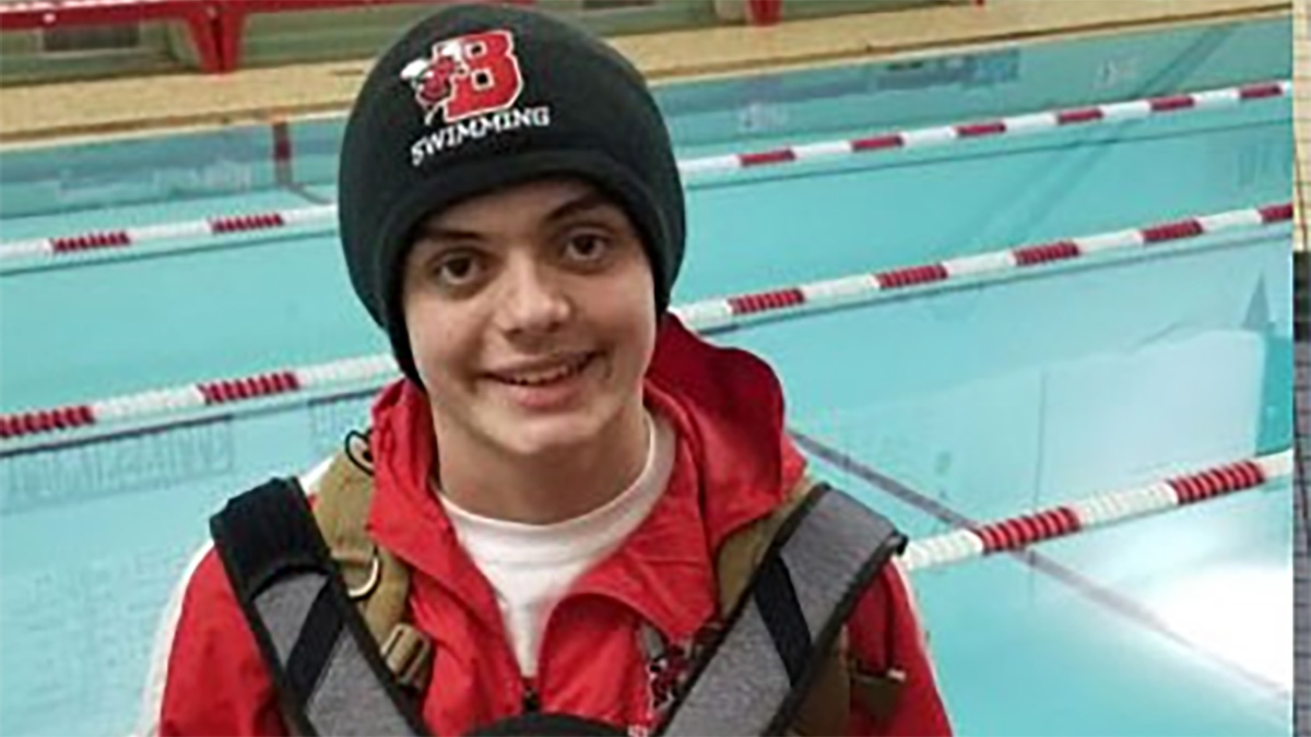 Mikey Mikey is a teenage boy standing in front of a swimming pool and wearing a backpack.