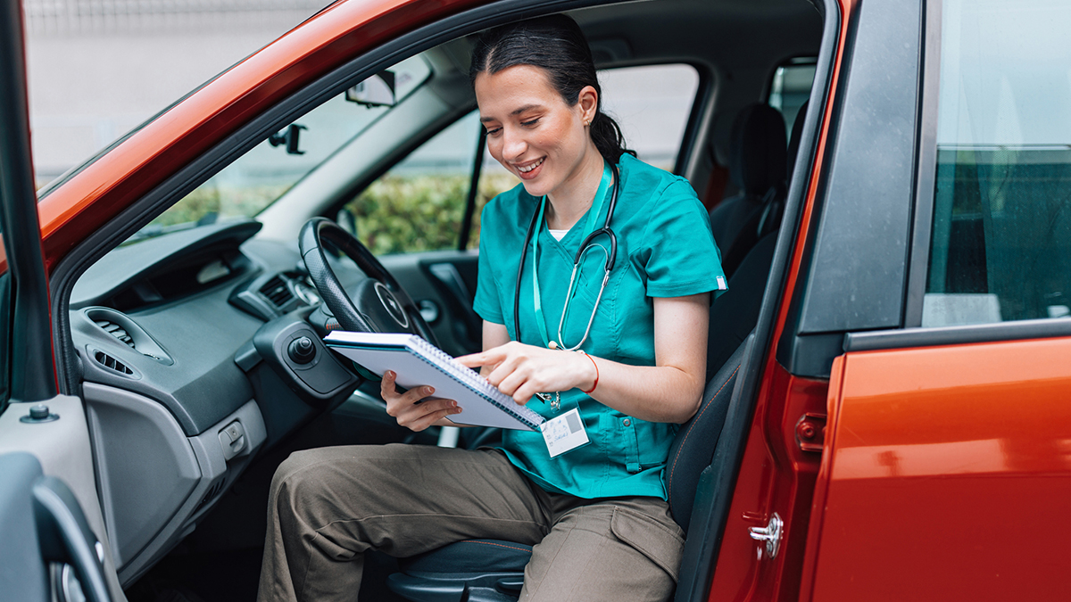 A health care professional getting out of her car while looking at her notebook