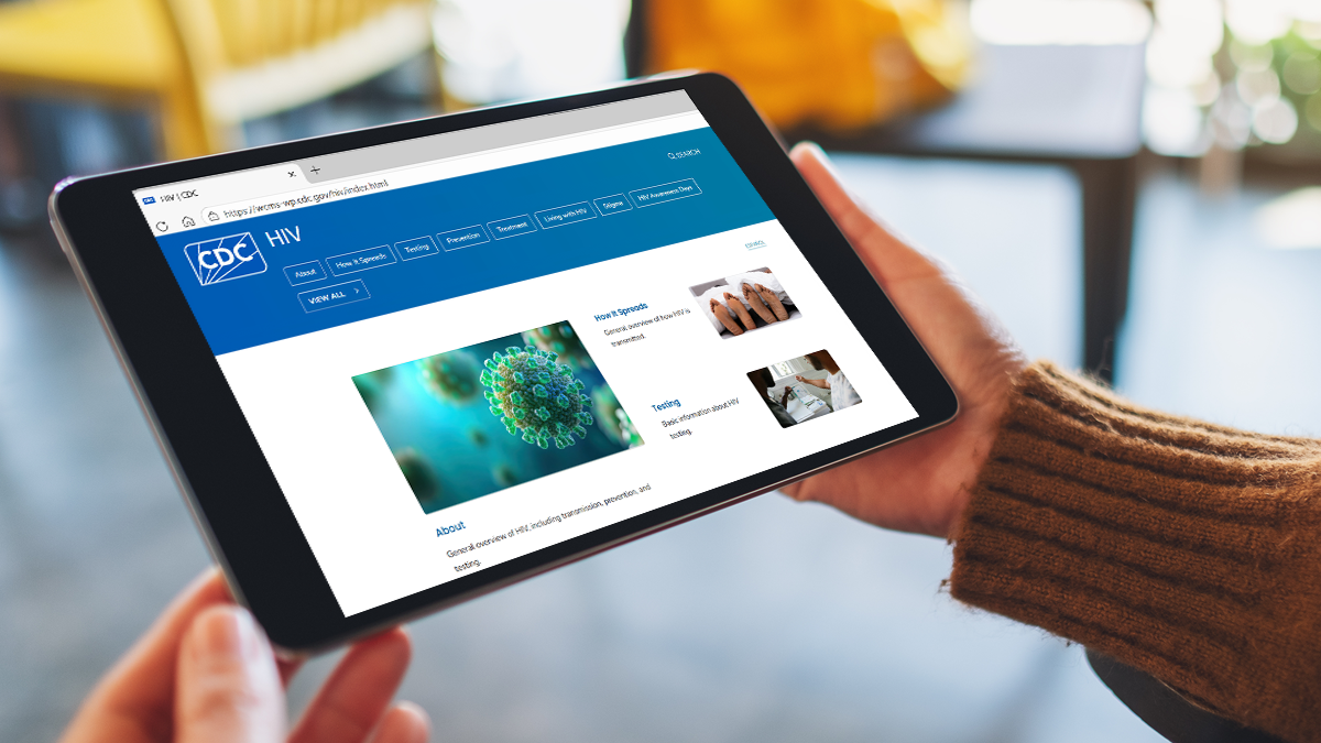 Two hands holding a tablet with the CDC HIV home page open.