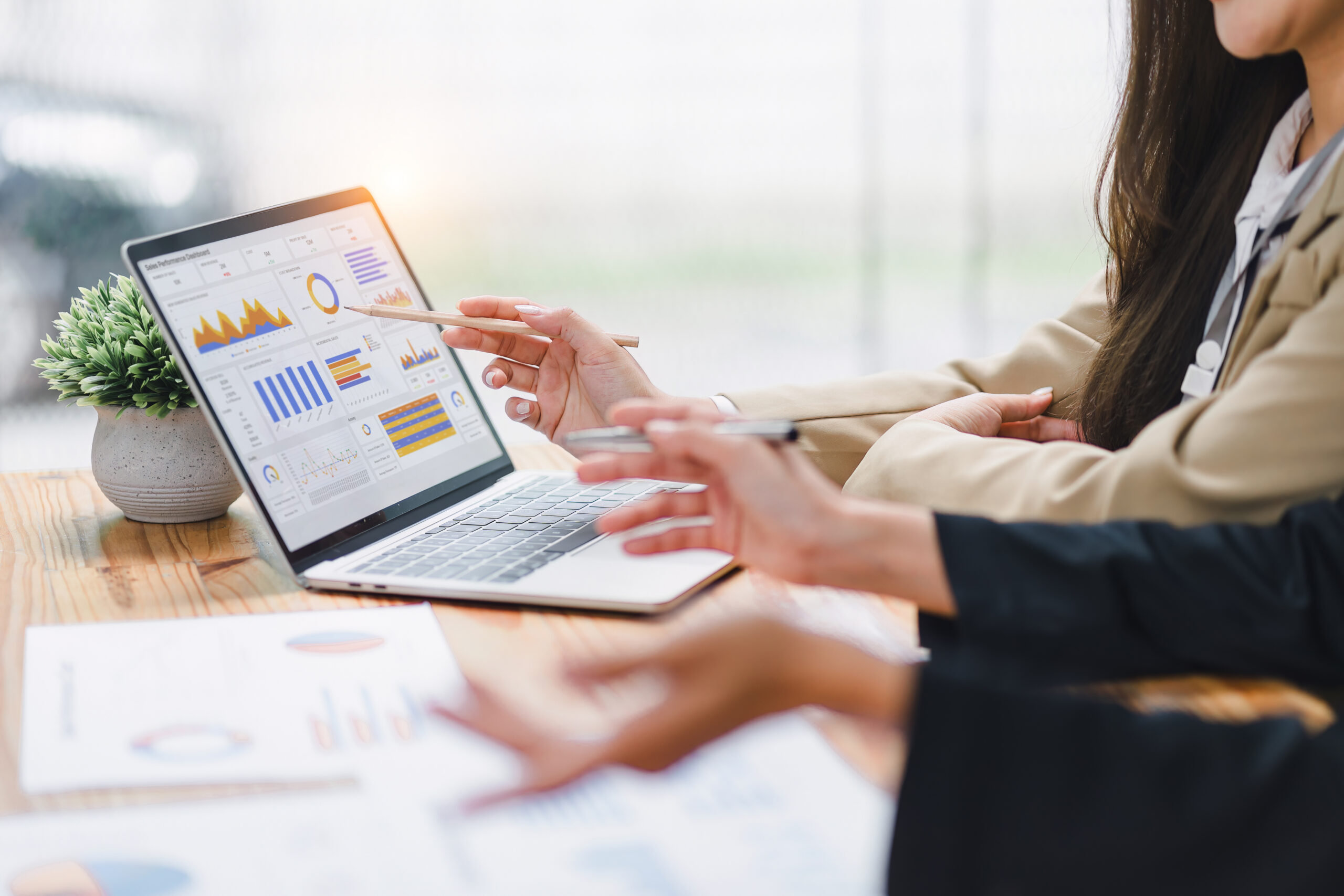 Two people are analyzing data charts, graphs, and a dashboard on a laptop screen
