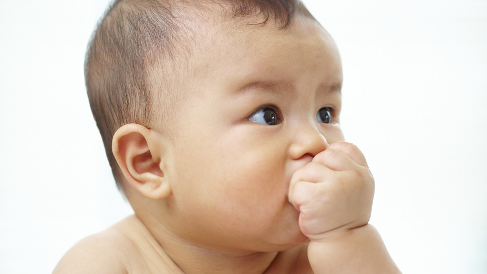 An infant putting their hand to their mouth.