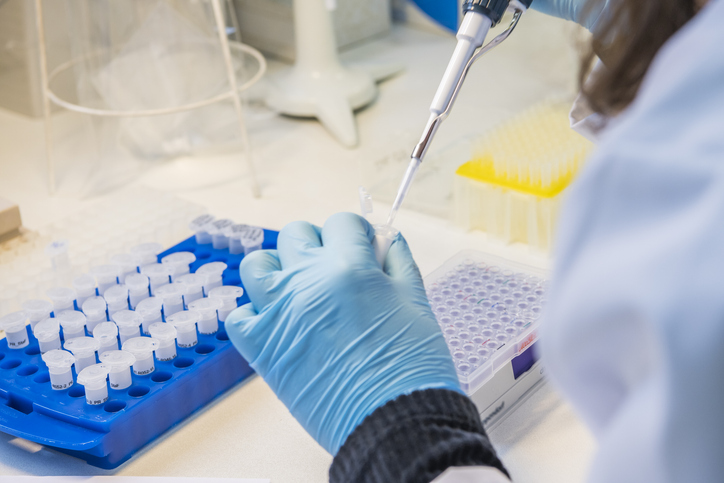 Scientist with blue glove puts a sample into a test tube to perform testing