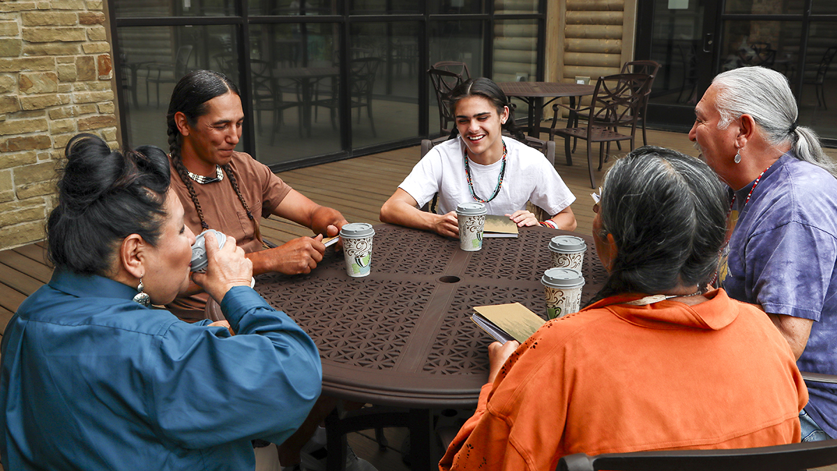 Community Book Club Five tribal adults sit around an outdoor table with coffee cups and books
