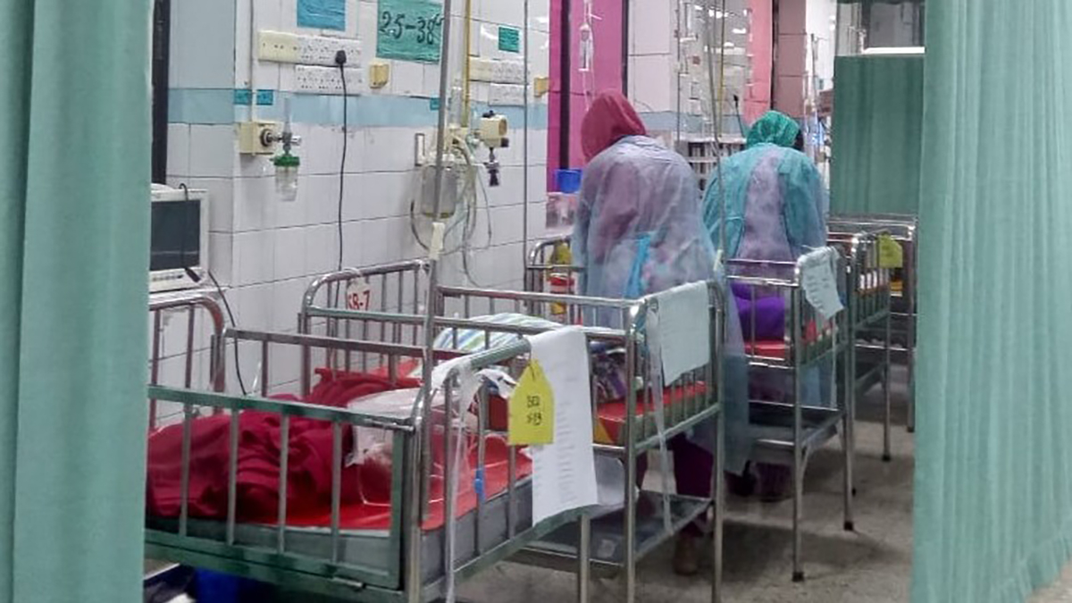 Two healthcare workers tend to infants in cribs in a NICU in Bangladesh.