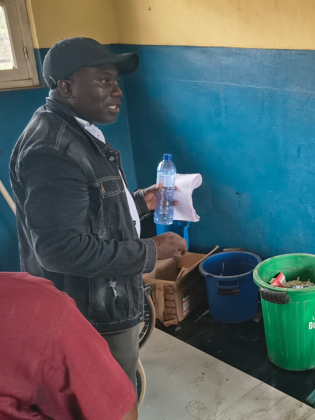 Man holding trash items and standing in front of several trash bins discusses proper waste management.