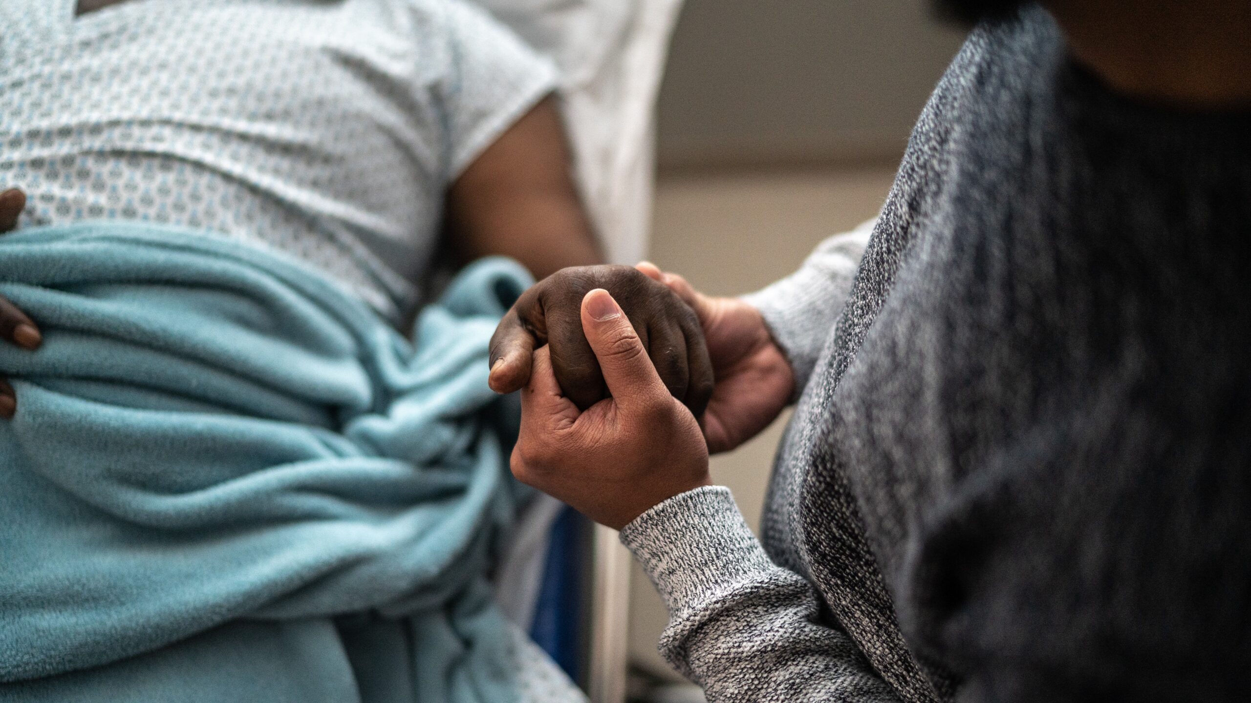 Patient holding hands with loved one in a hospital bed.