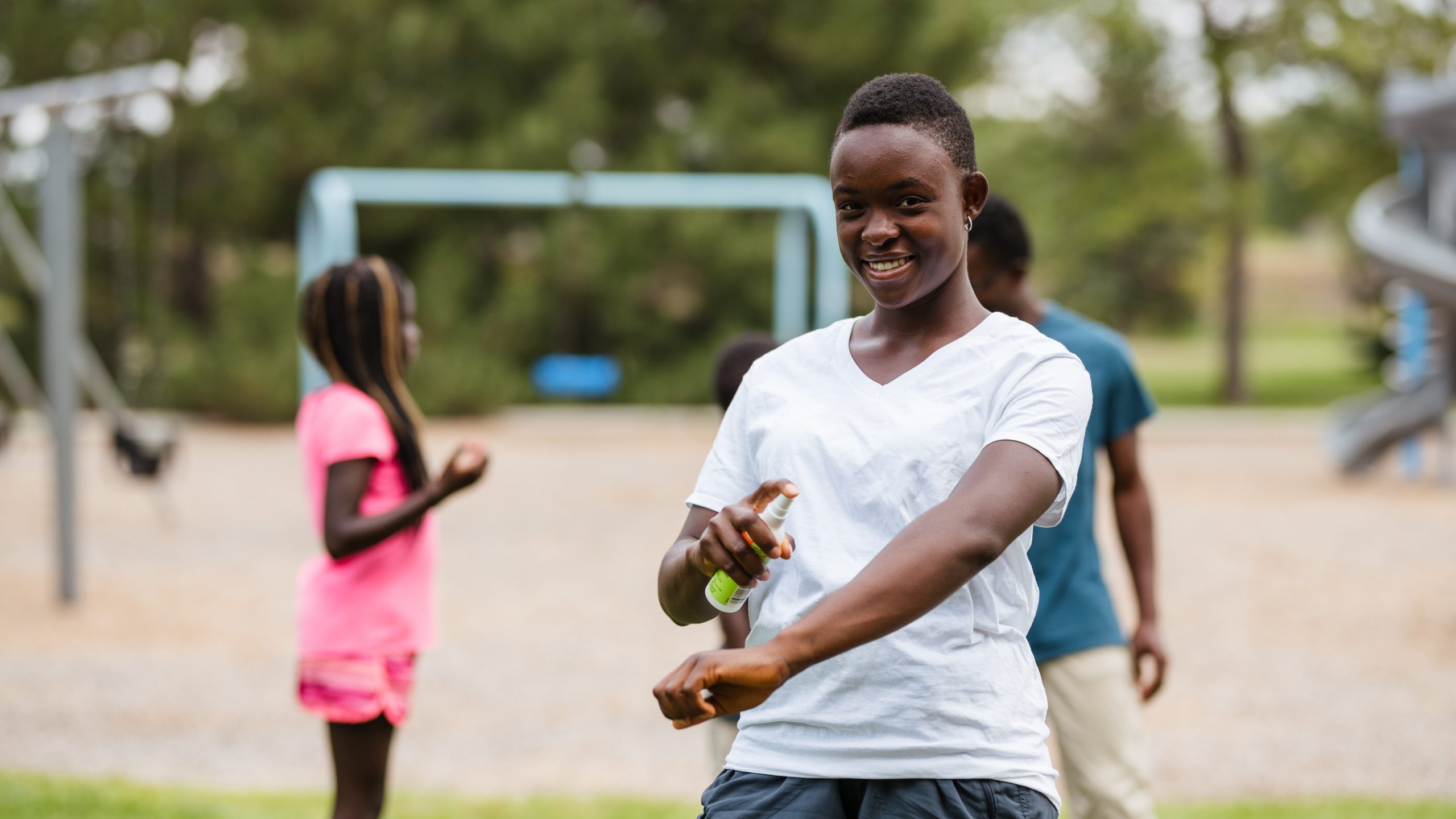 Young man at a playground applying insect repellant to his arm.