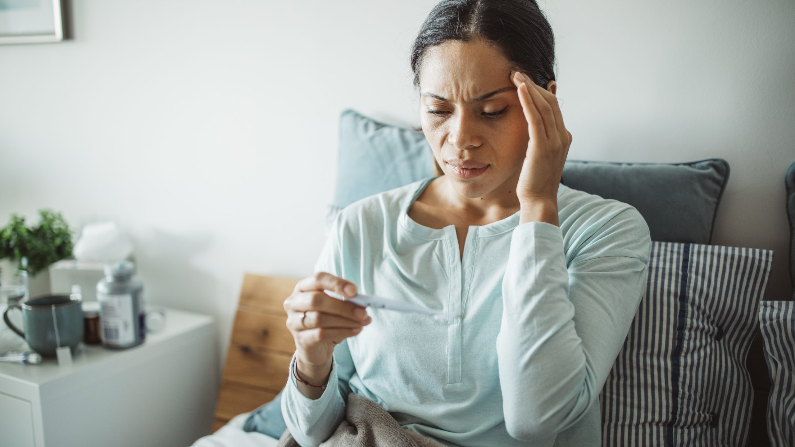 A woman with headache examines a thermometer.