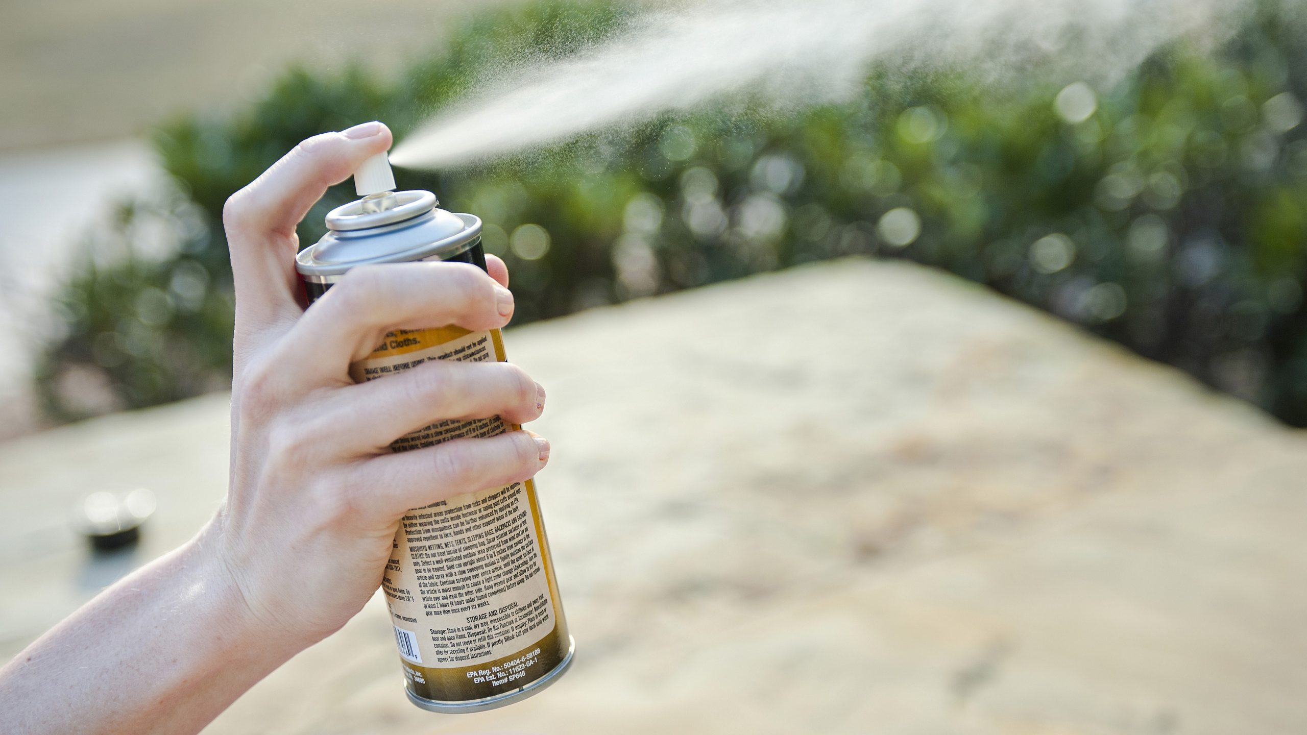 Hand spraying insect repellent into the air outdoors.