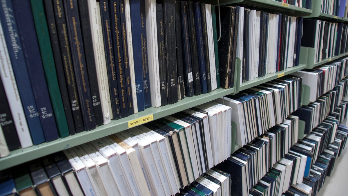 Stacks in a library filled with books and reports.