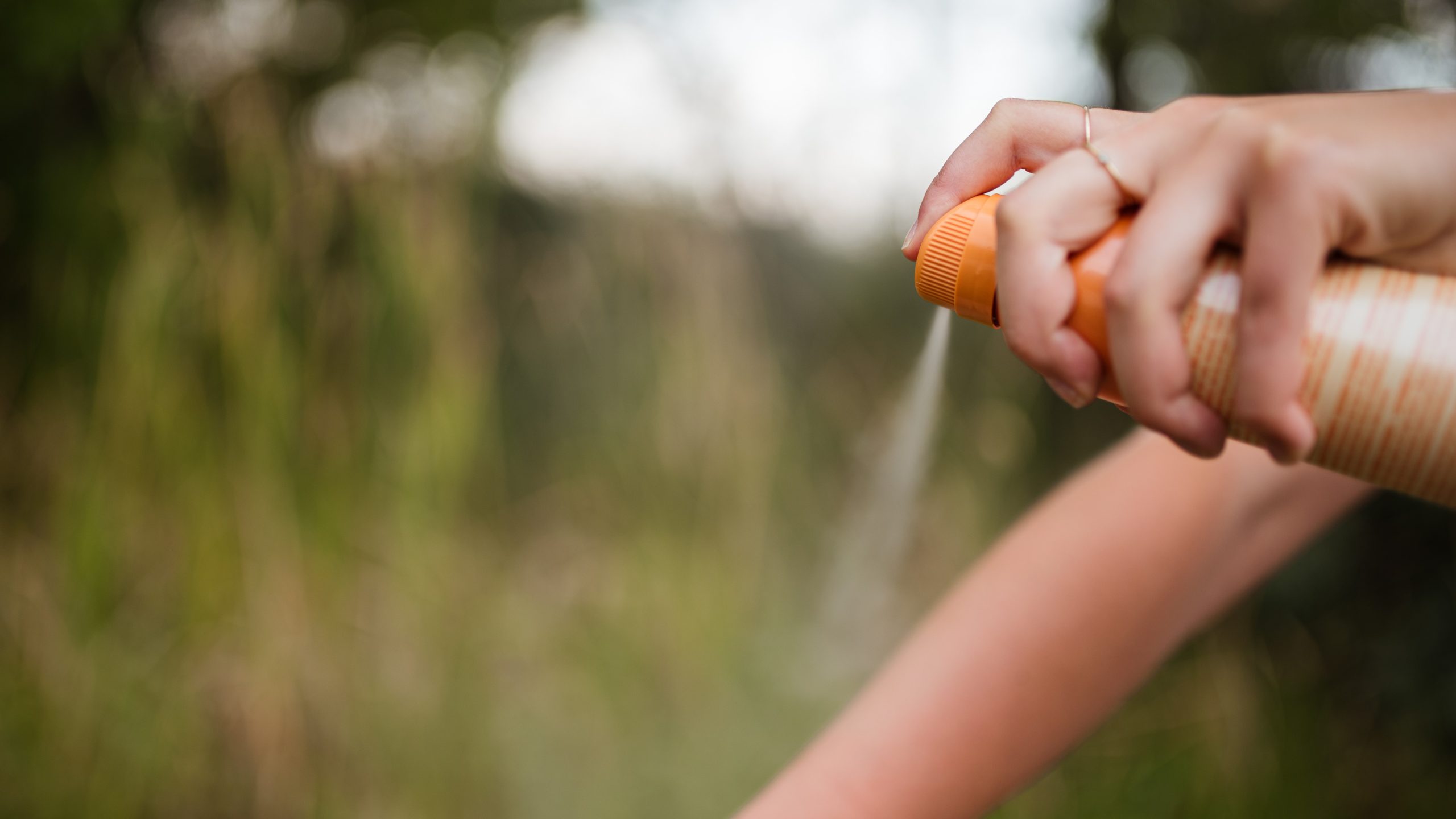 A person applies insect repellent to their arm.