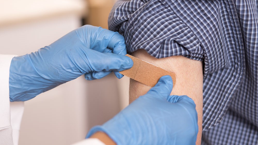 A healthcare professional places an adhesive bandage on person's arm following vaccination.