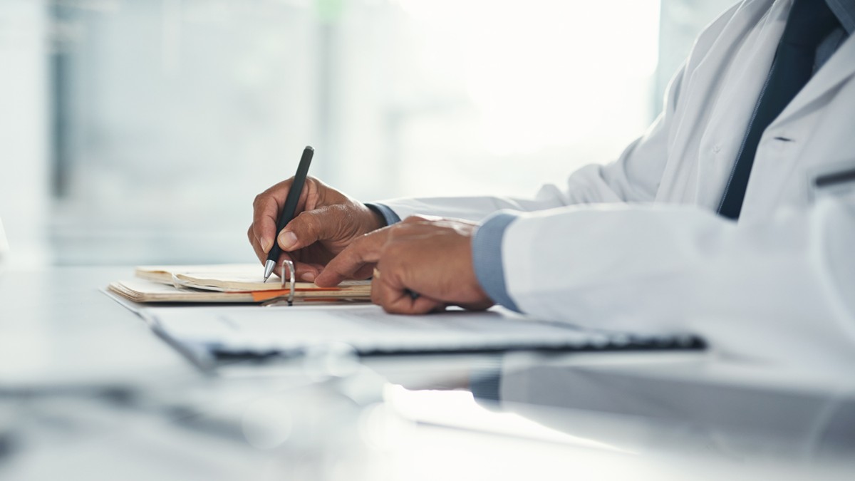 Doctor hands writing on paper at a desk at a healthcare facility.