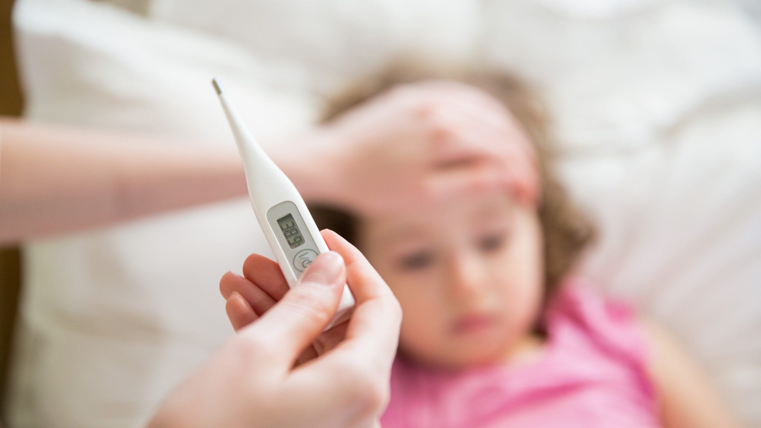 A parent places a hand on a child's forehead while examining a thermometer.