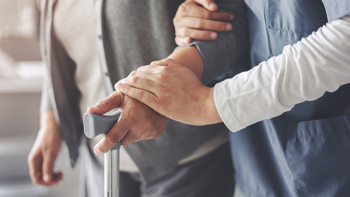 The nurse is helping the old patient with a cane