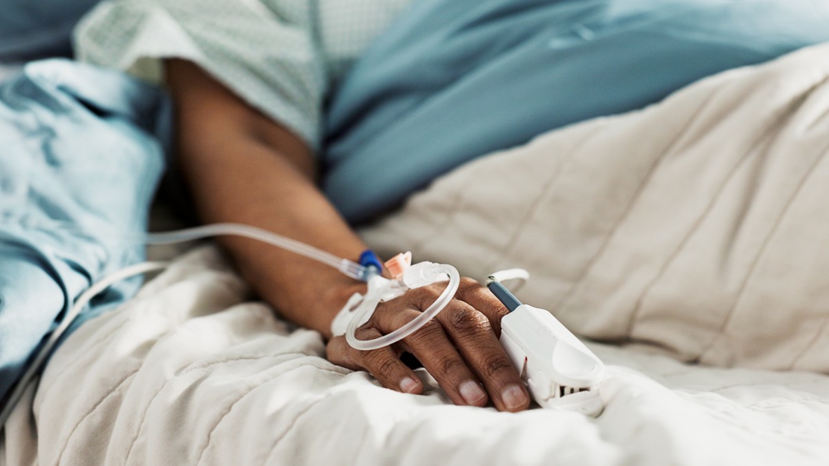 A patient lies in a hospital bed with an IV inserted.