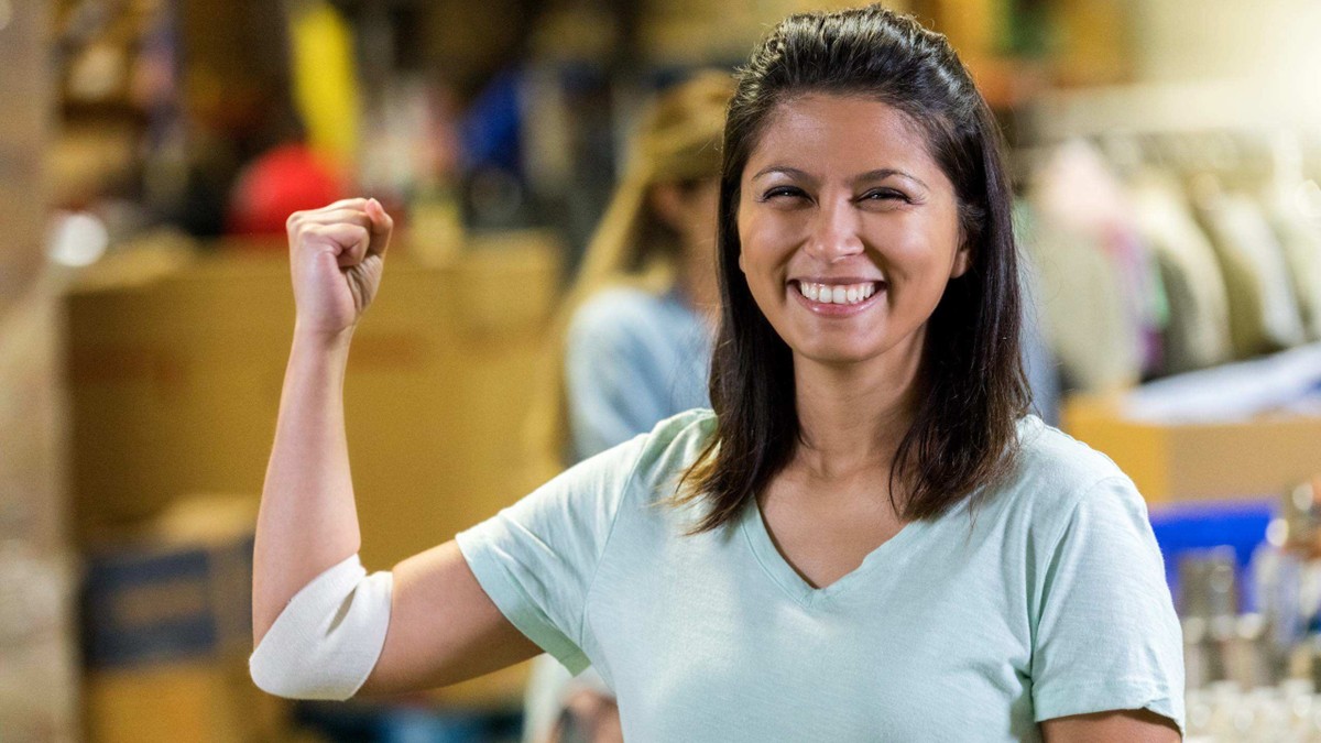 A smiling woman flexes her arm muscle after donating blood at a clinic.