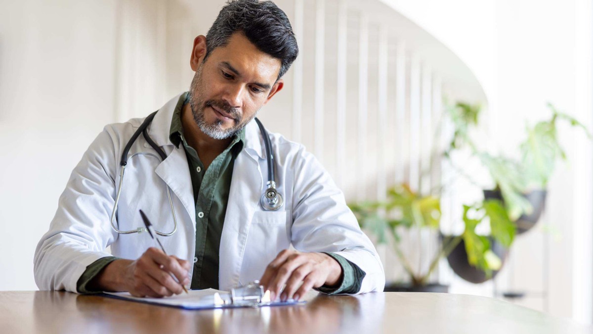 A male doctor at a desk writes on a medical chart.