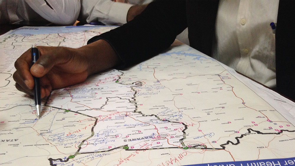 Hand holding pen marking locations on a map