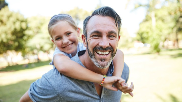 Father with his daughter riding on his back and her hands around his neck.