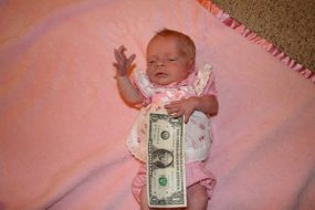 Baby Brenna dressed in doll&rsquo;s clothes, half-covered by a 1- dollar bill