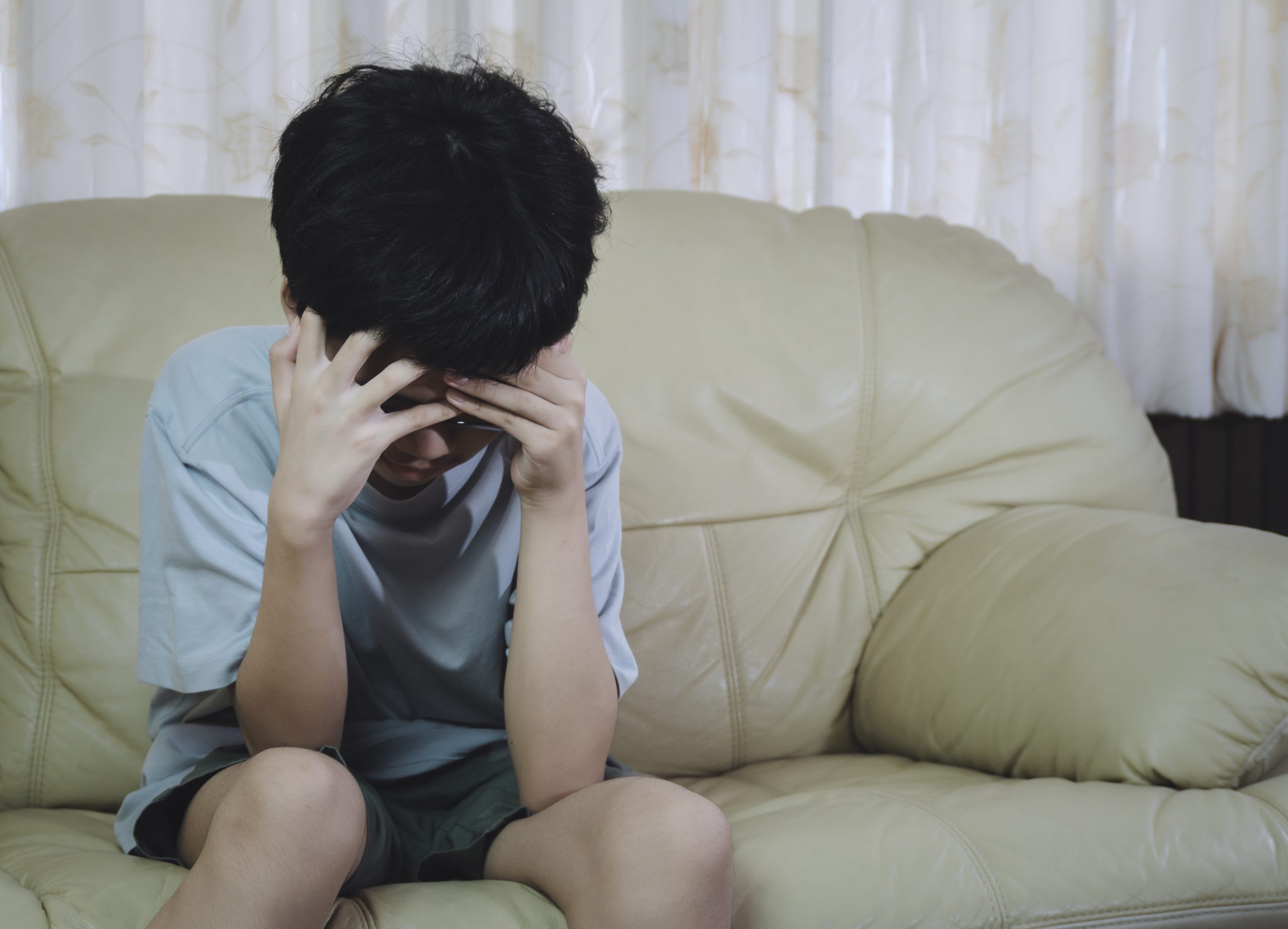 Un ni&ntilde;o sentado en un sof&aacute; con la cabeza entre las manos.