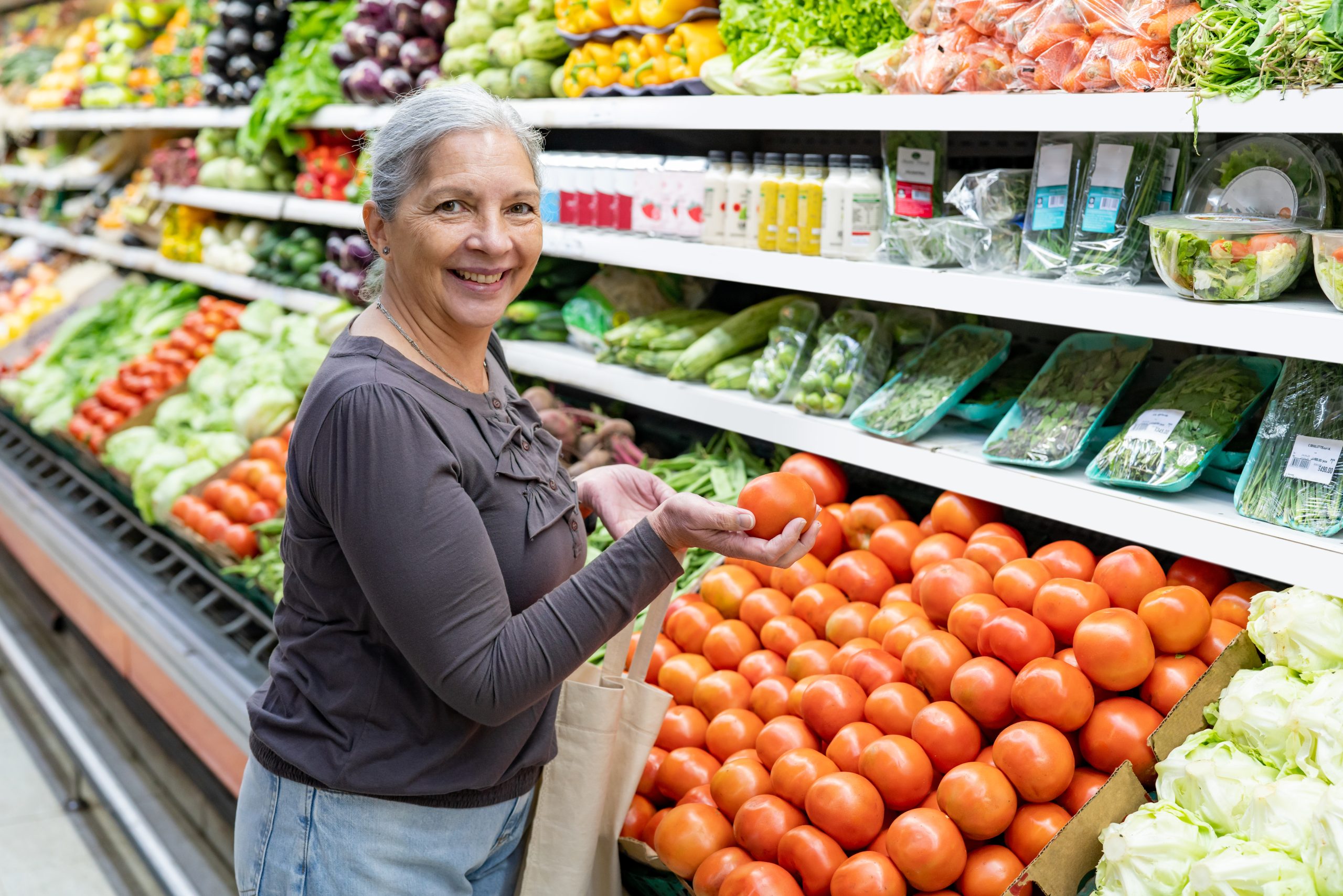 Women buying produce Woman looking at the camera while holding a tomato in the produce section of the grocery store.