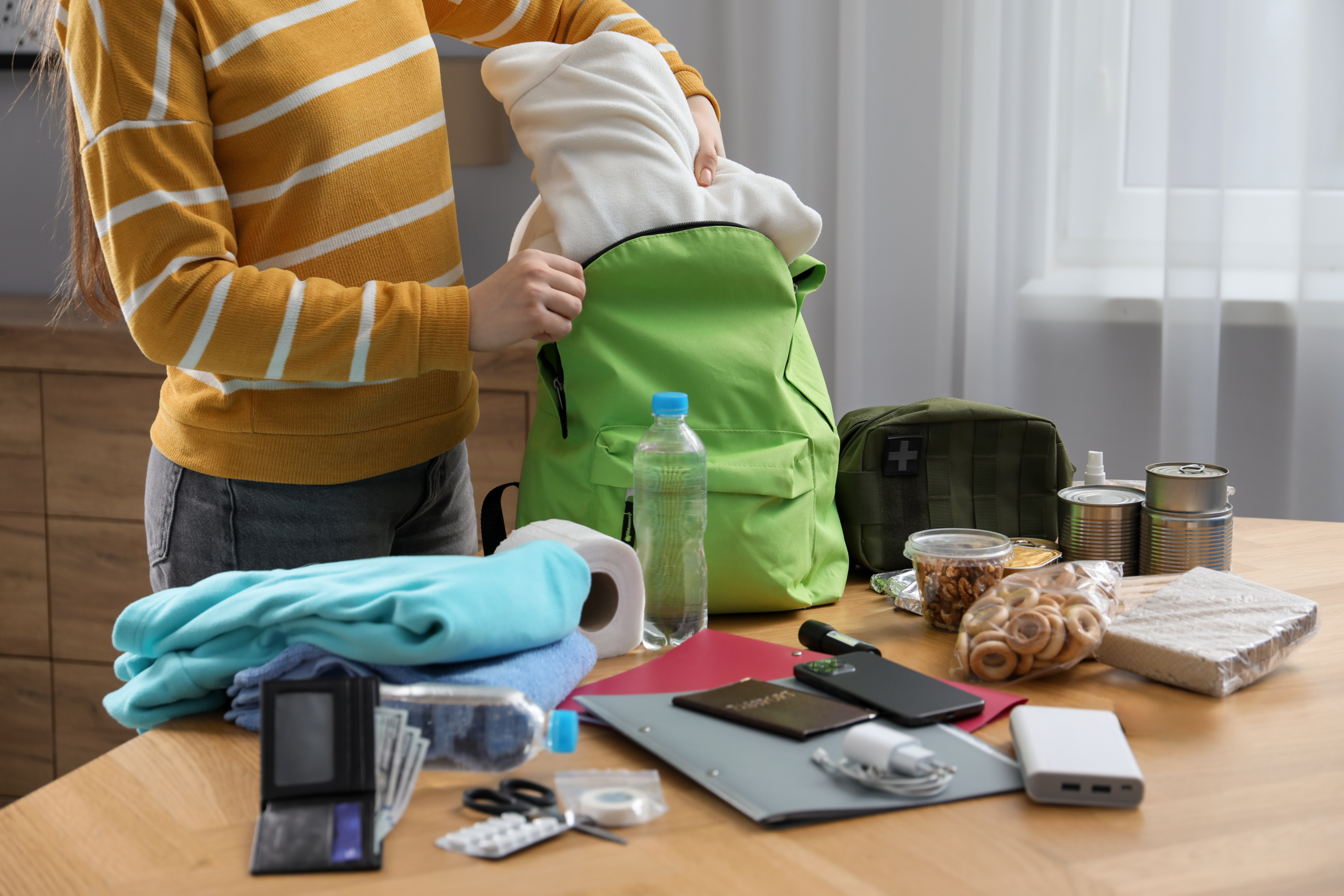 Teen with emergency supplies gathered on a table and putting them into a backpack.