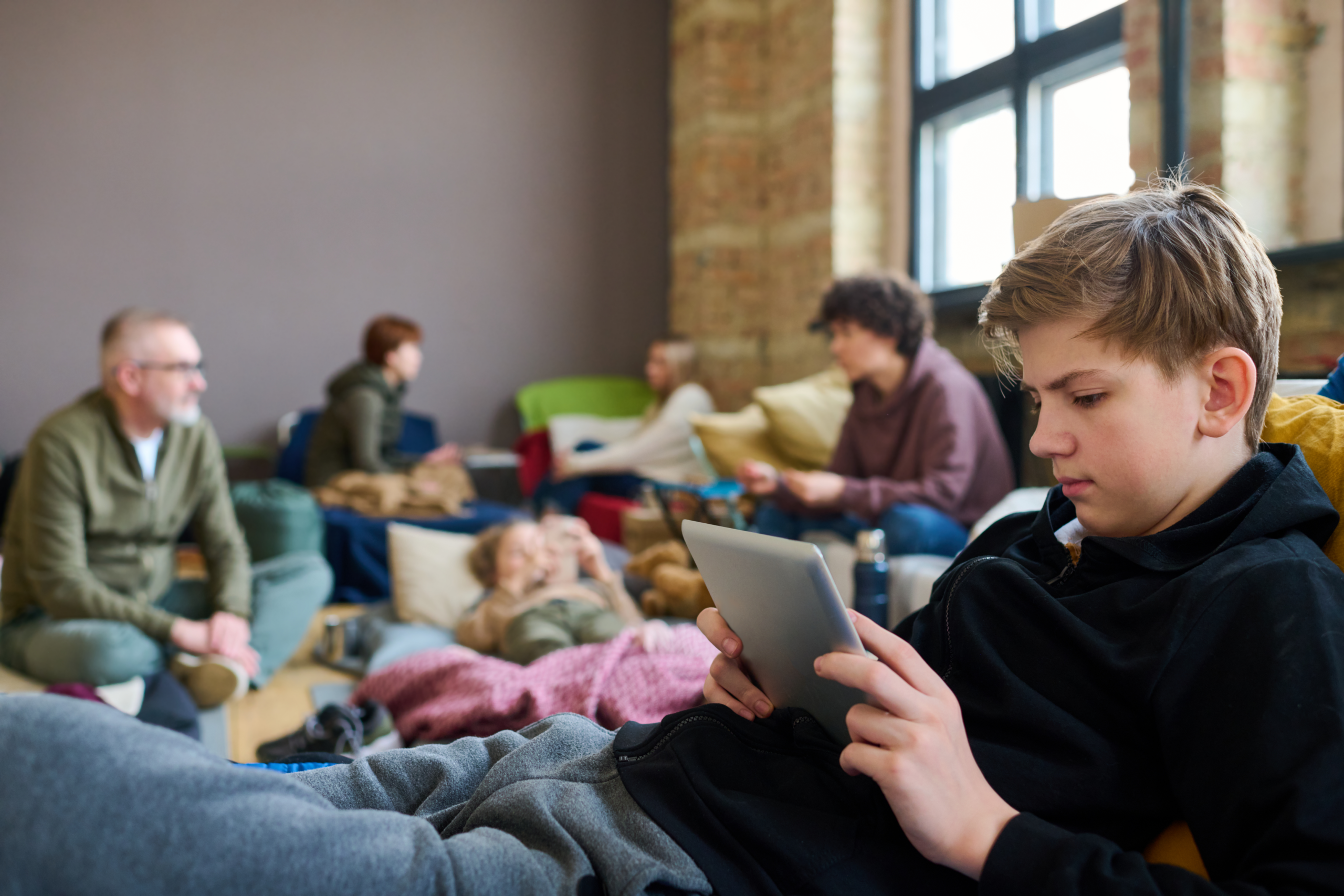 Teen boy is using a tablet while at a disaster shelter.