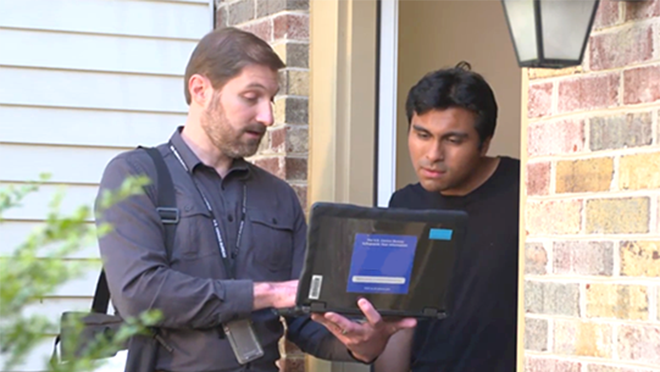 Man standing with laptop and interviewing another man at his front door