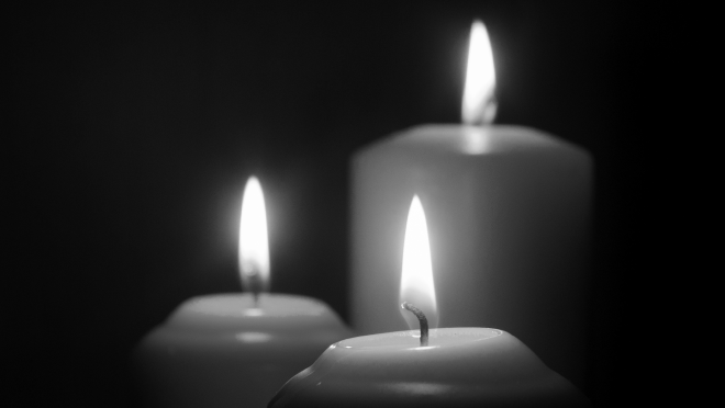 Black and white image of three candles burning in front of a black background