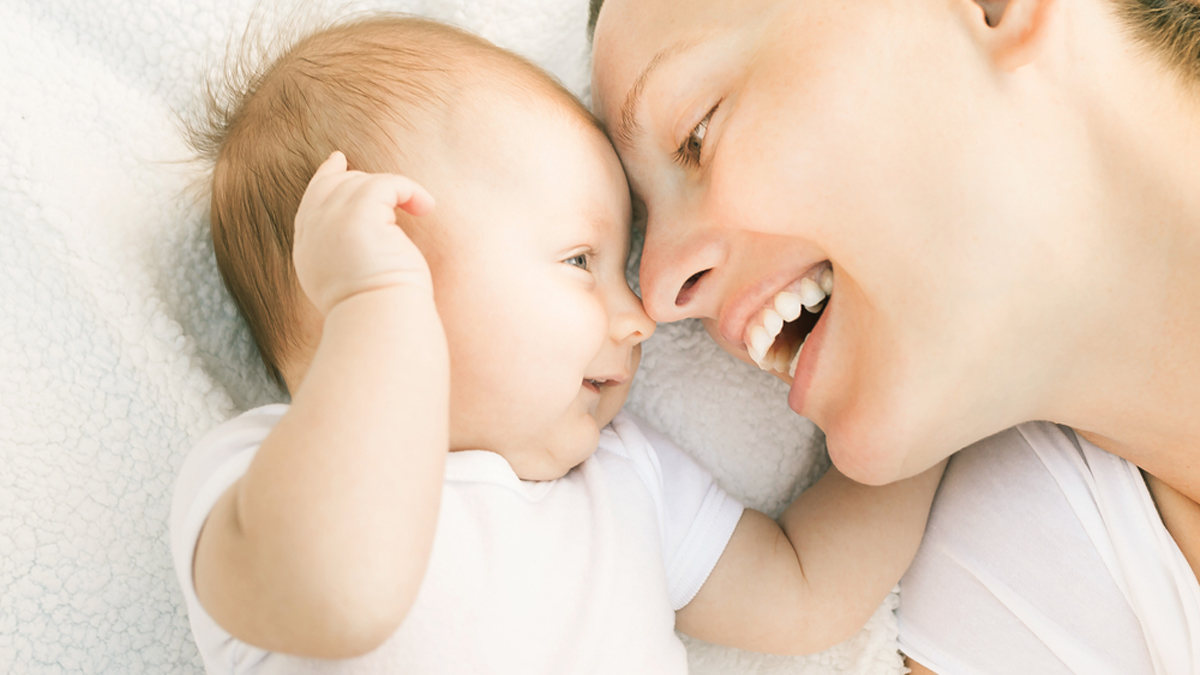 Mother and baby lie in bed, foreheads touching