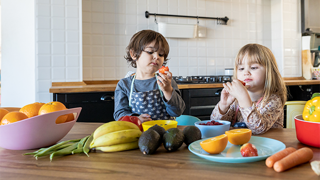 A little boy and a little girl sitting at a table eating fruit.