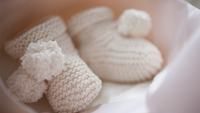 A pair of white baby booties sitting inside a gift box with white tissue paper.
