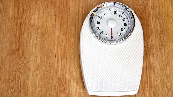 A white mechanical scale sitting on a hardwood floor.