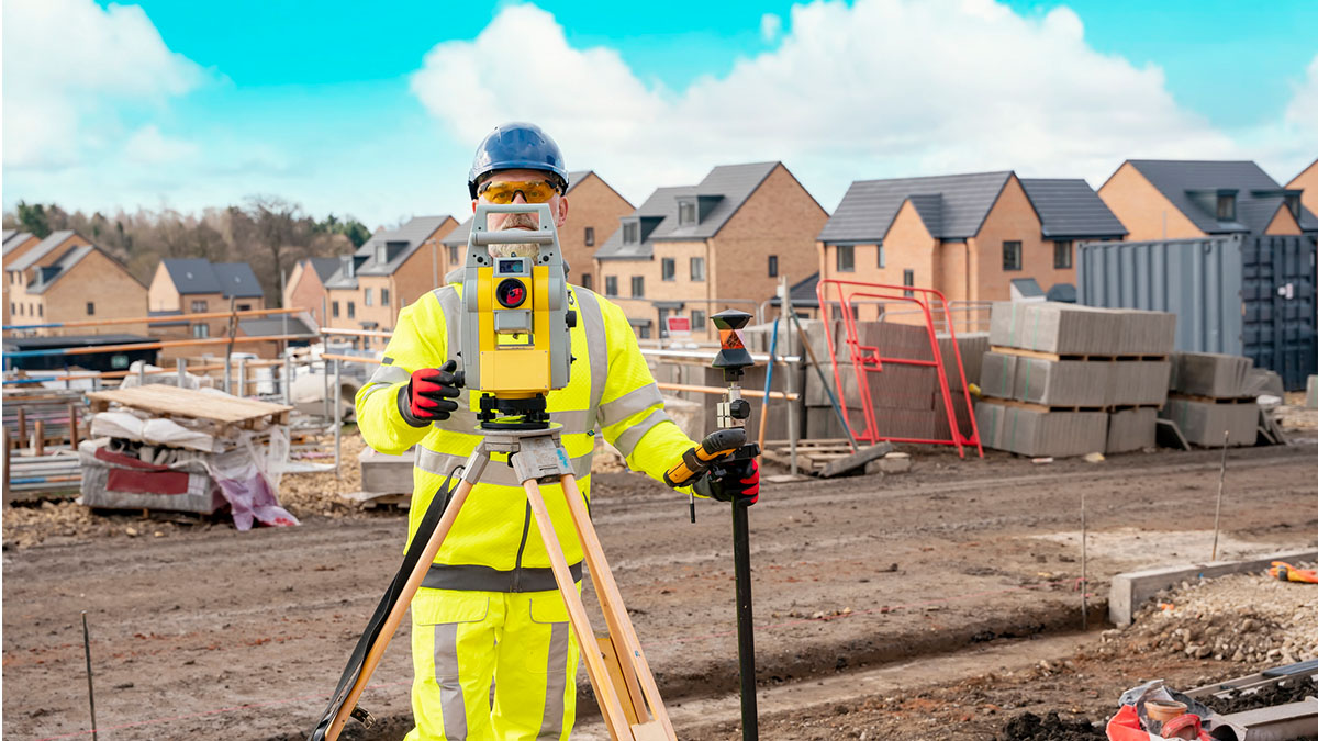 Trabajador de la construcción con equipo de protección individual realizando labores de topografía en una obra.