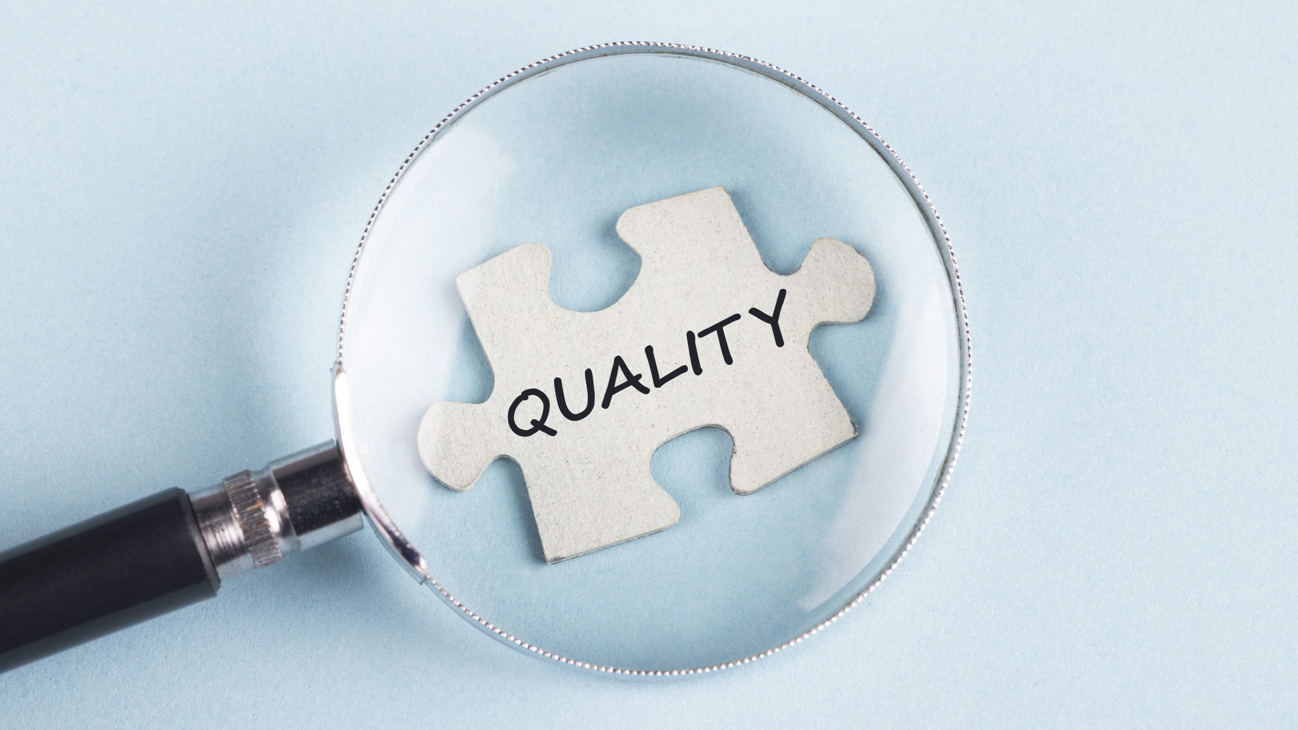 Quality assurance A magnifying glass over a puzzle piece with the word "Quality" on it.