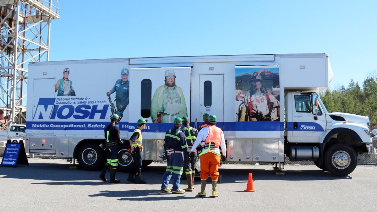 Coal miners approach white and blue mobile heath unit for black lung screenings.