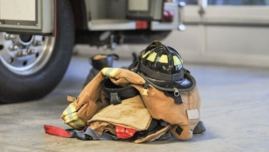 Photo of fire gear, helmet, jacket etc., in a pile on the ground by the tire of a fire truck