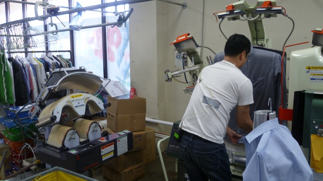 Man in a white t-shirt, working in a dry cleaning shop, with a sensor taped to his shirt.