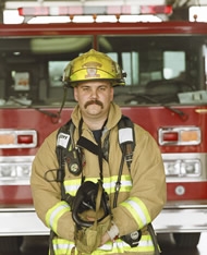 Photo of a male firefighter in gear standing in front of a fire truck
