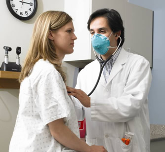 Male doctor wearing a respirator examining a female patient.