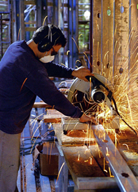 Male worker using a saw with hearing protection and a respirator.