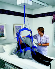 Healthcare worker using a lifting device on a patient in a bed.